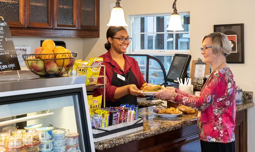 Rosewood cafe worker handing a senior woman a plate of food