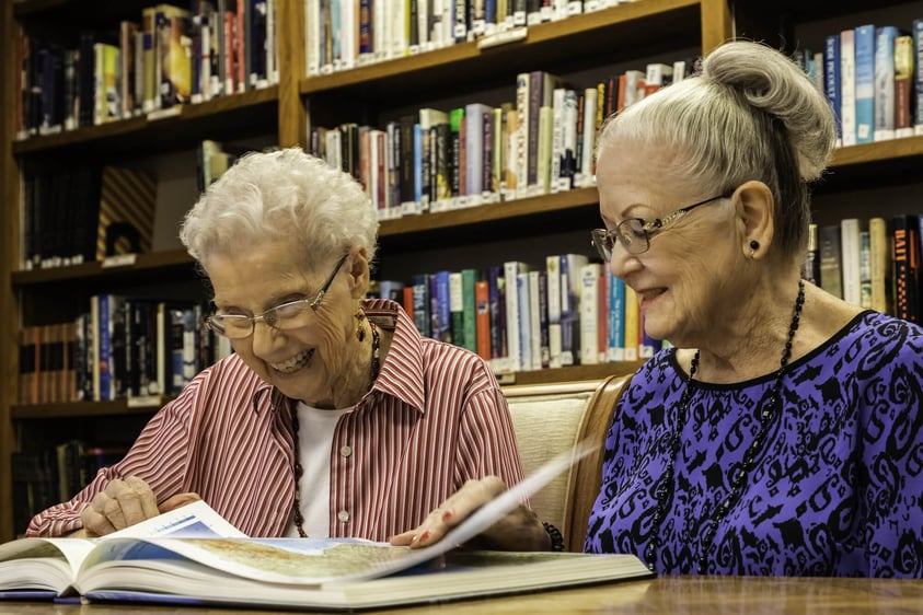Two senior women looking at a book in the library at Rosewood