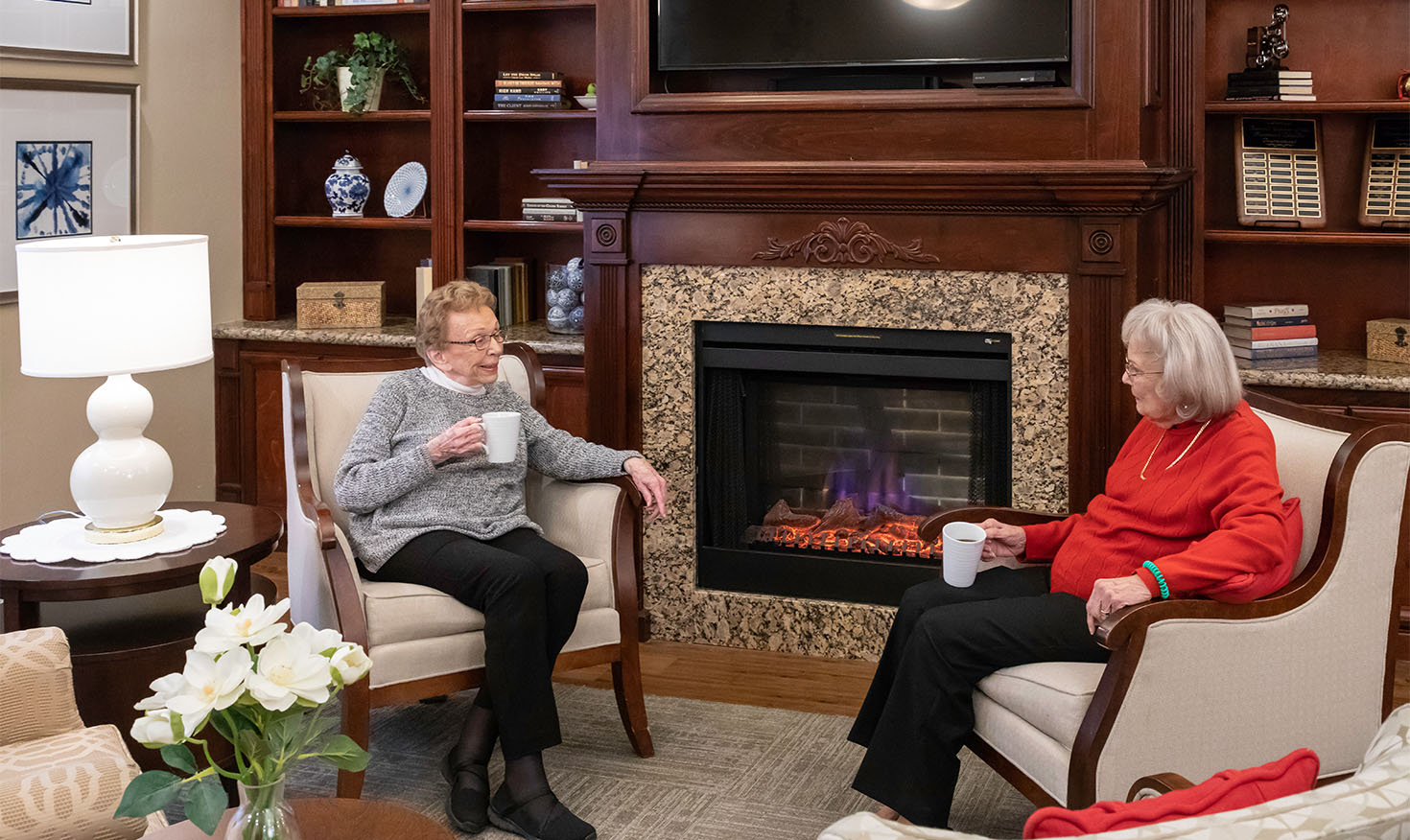 Two senior women having coffee together next to a fireplace at Rosewood