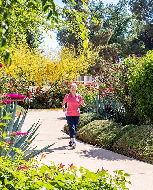 Senior woman walking on a sidewalk through the garden at Rosewood
