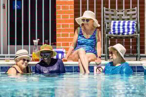 Four seniors wearing sun hats and lounging in and by the pool at Royal Oaks