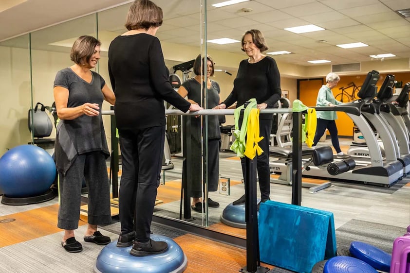 Senior woman standing on a BOSU ball in front of a mirror in the fitness center at Royal Oaks