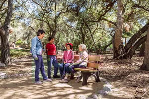 Two senior woman standing talking to two senior women sitting on a bench off a trail at Royal Oaks