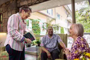 Senior woman holding a book talking to senior couple sitting in armchairs in a lounge area at Royal Oaks