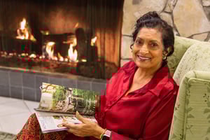 Senior woman holding a magazine and sitting by a fireplace 