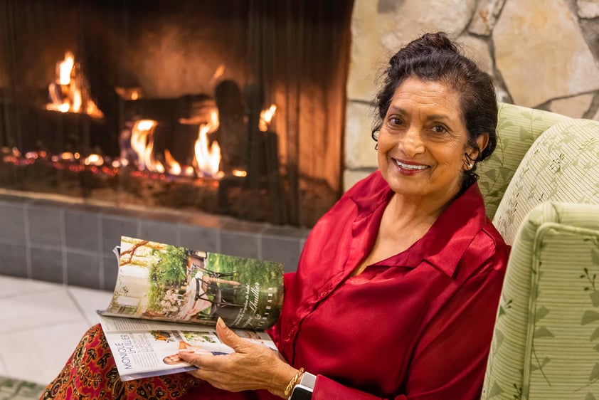 Senior woman holding a magazine and sitting by a fireplace 