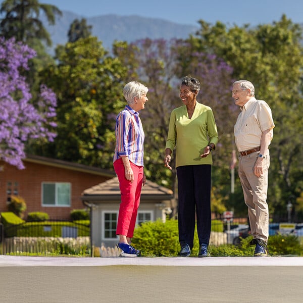 Two senior women and a senior man standing outside at Royal Oaks and chatting with the mountains in the background