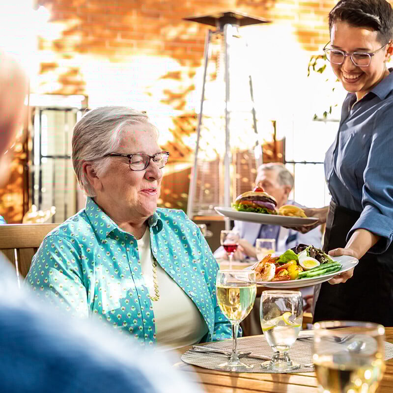 Dining room team member serving dinner to a senior woman