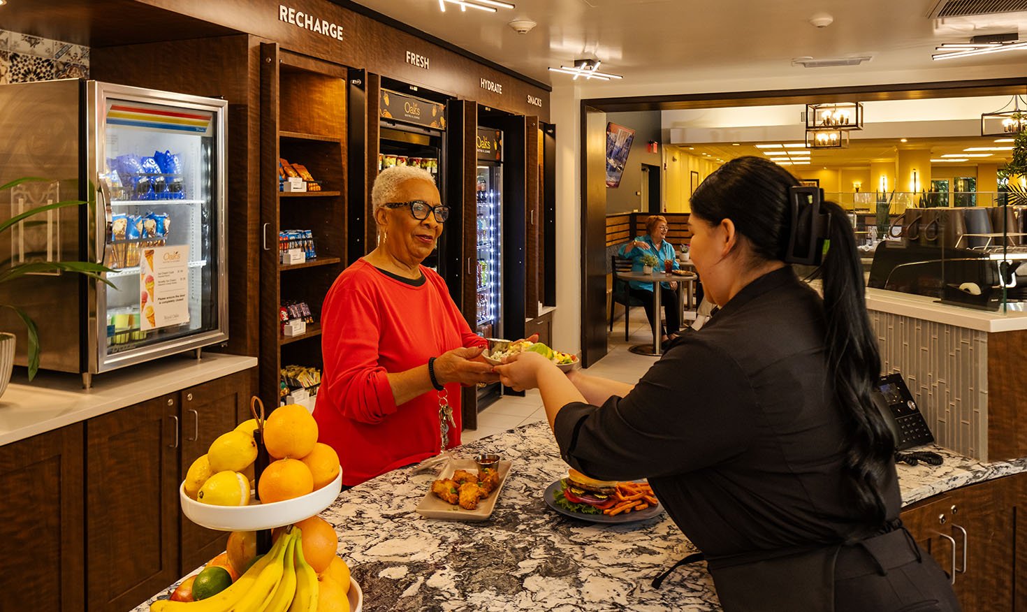 Team member handing a plate to a senior woman in the bistro at Royal Oaks