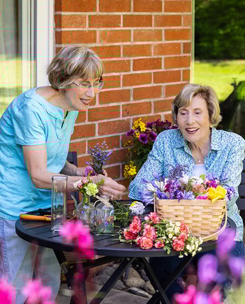 Two senior women at a patio table arranging flowers