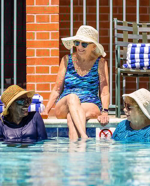 Three seniors wearing sun hats and lounging in and by the pool at Royal Oaks