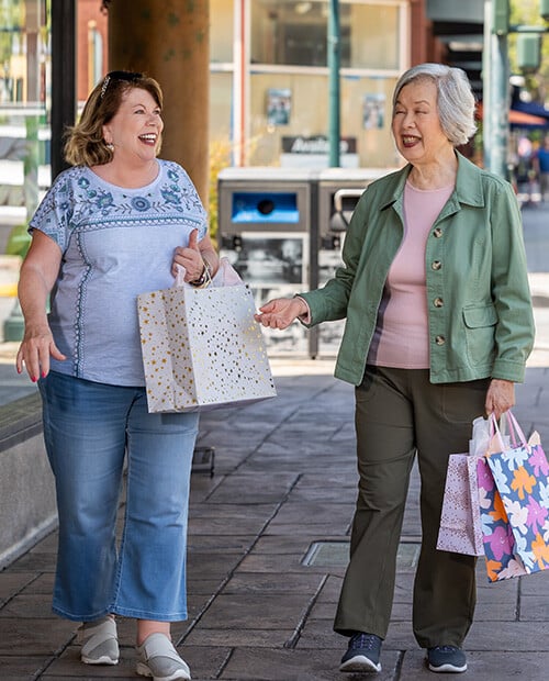 Two women holding shopping bags and walking down the sidewalk