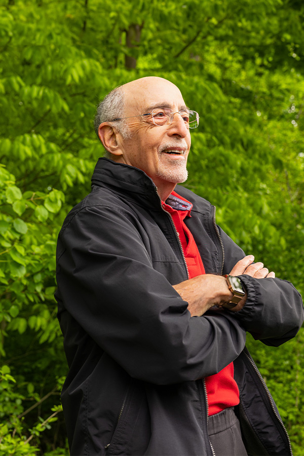 Smiling senior man wearing glasses standing outside with his arms crossed 
