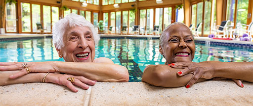 Two smiling senior women learning against the edge of a swimming pool