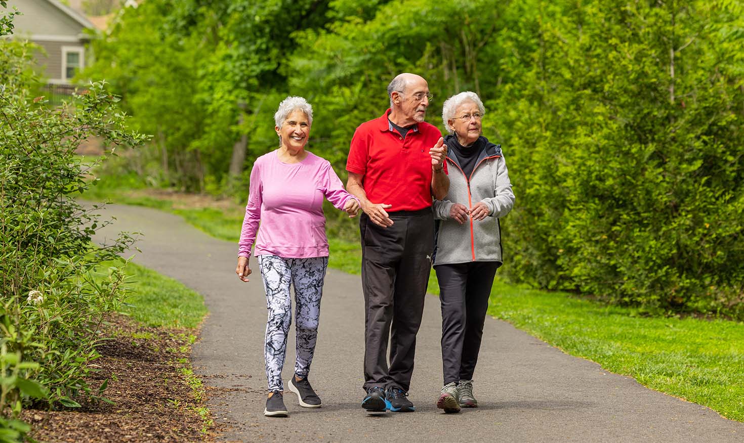 Two senior women and a senior man walking on a paved path