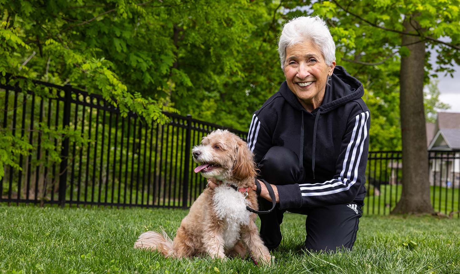 Senior woman in a track suit posing outside with a small dog outside