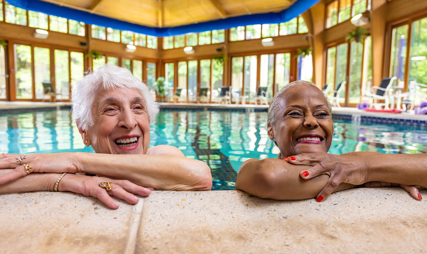 Two smiling senior women learning against the edge of a swimming pool