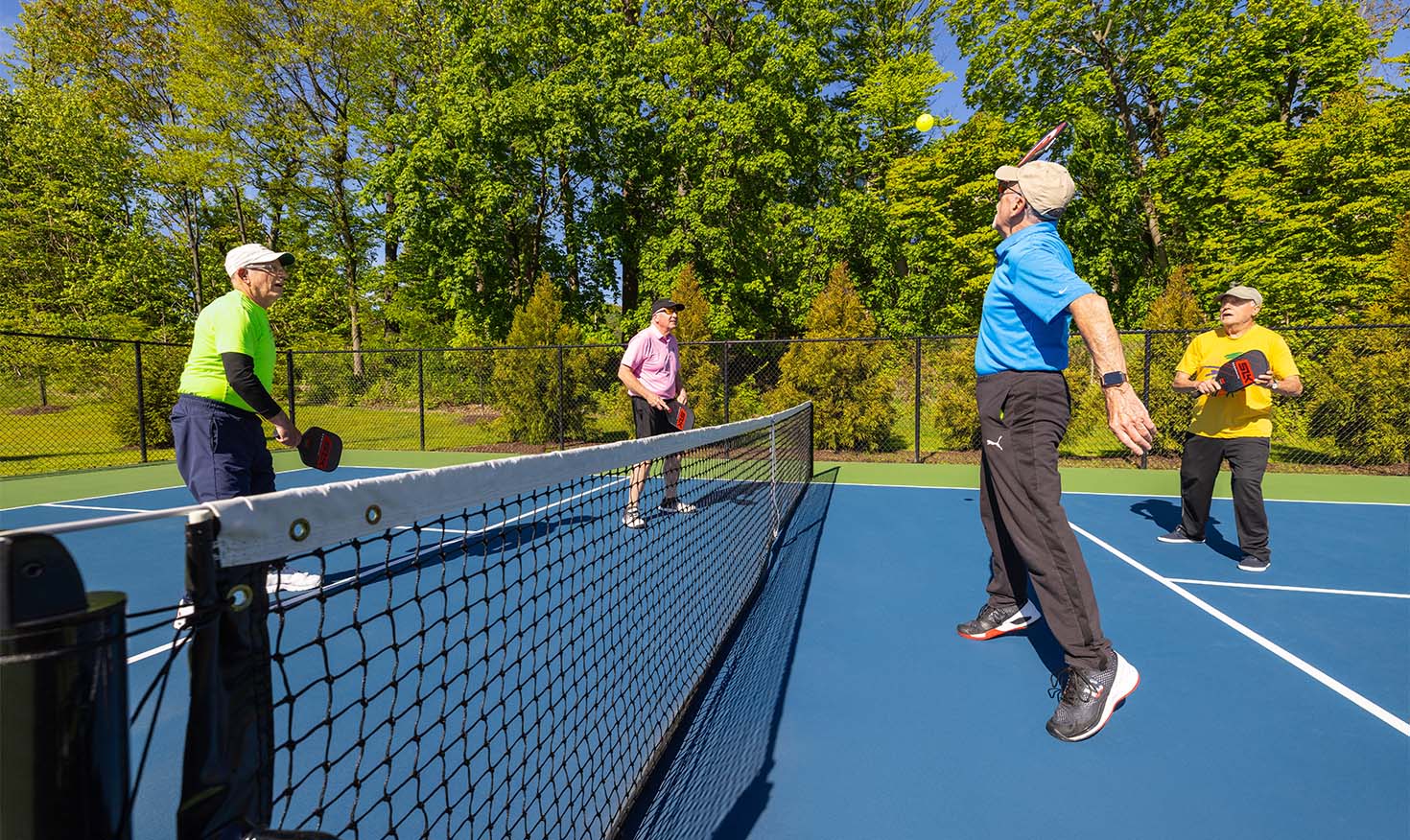 Four senior men playing pickleball on an outdoor court