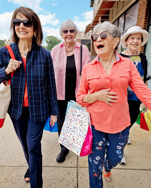 Group of four senior women walking outside with shopping bags