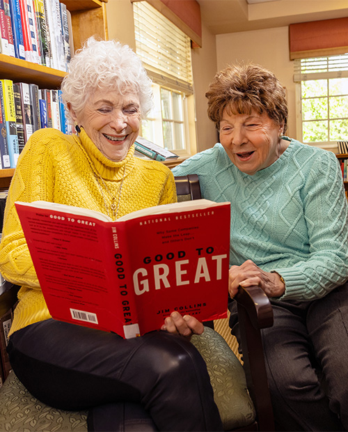 Two senior women reading a book inside the library