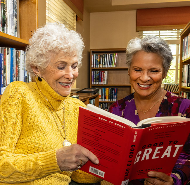 Two senior women reading a book at the library