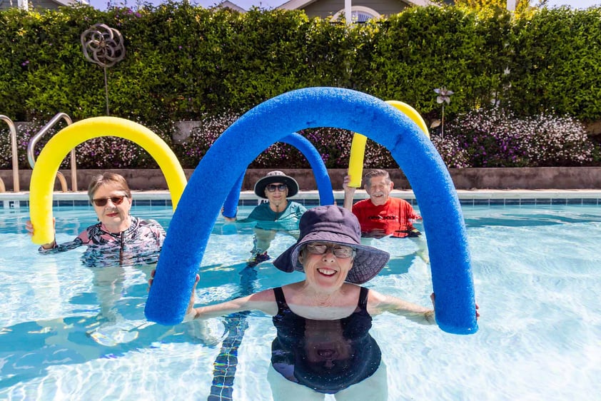 Group of four seniors in the pool holding up foam pool noodles