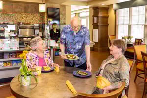 Senior man serving two senior women lunch in the bistro at The Terraces at Los Altos