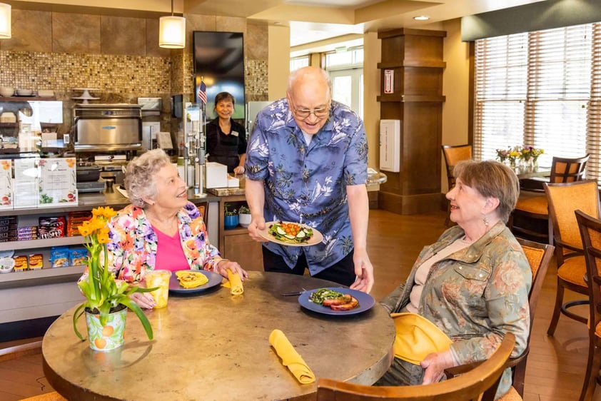 Senior man serving two senior women lunch in the bistro at The Terraces at Los Altos