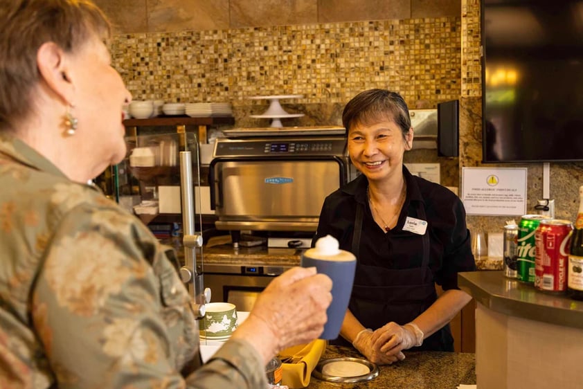 Senior woman getting coffee from a smiling team member in the bistro at The Terraces at Los Altos