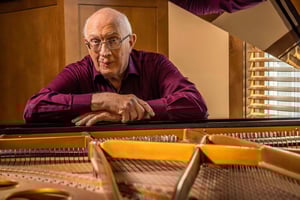 Senior man with his arms folded on top of a piano