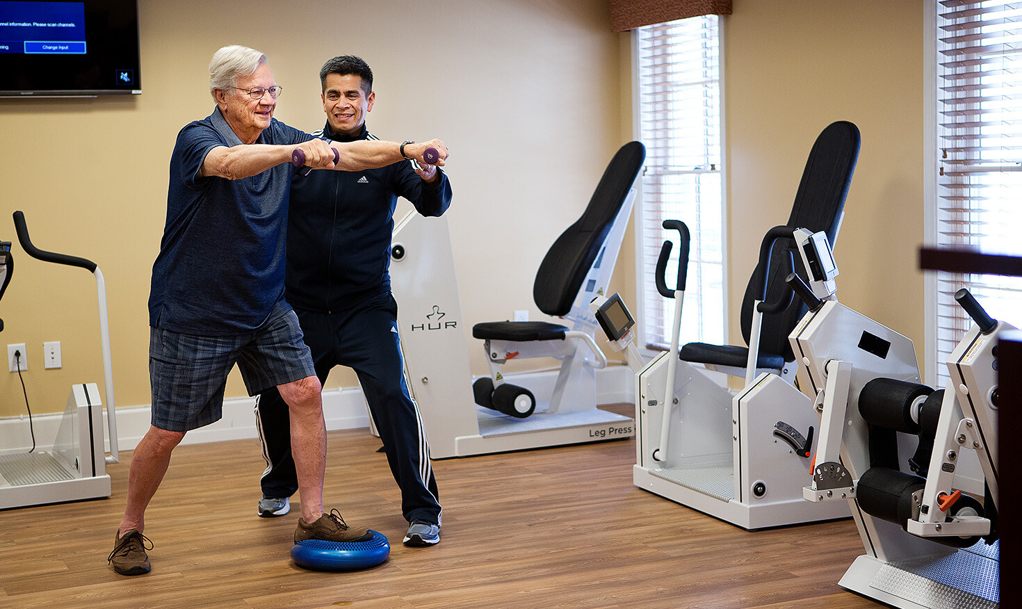 Senior man using light weights and working with a personal trainer in the community fitness center