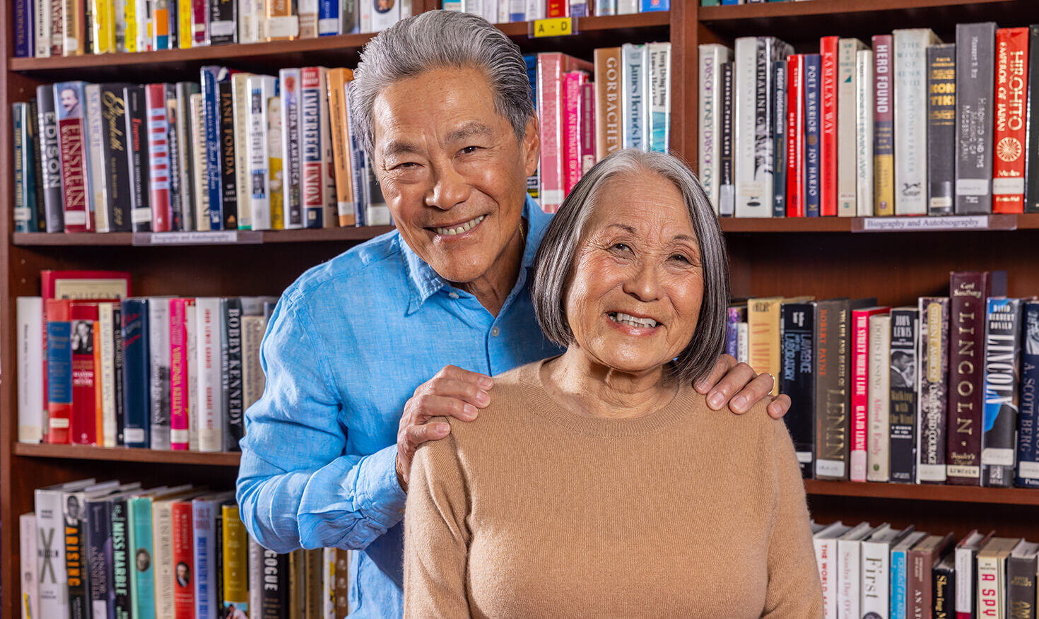 Senior man with his hands on the shoulders of a senior woman in front of a bookshelf in the library
