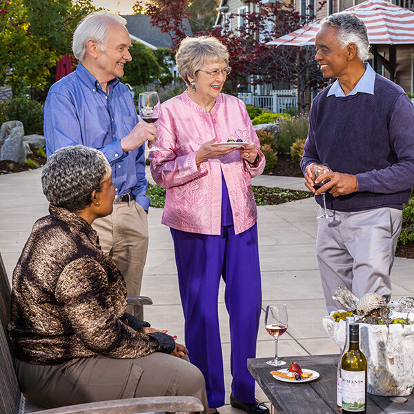 Two senior men and two senior women holding wine glasses and small plates of food on a patio