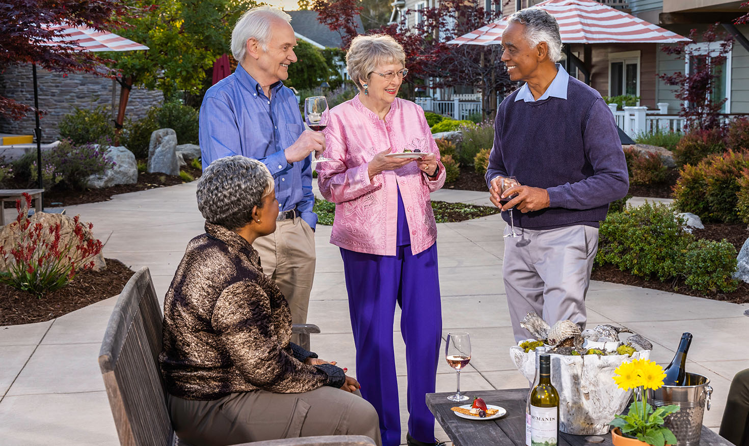 Two senior men and two senior women holding wine glasses and small plates of food on a patio