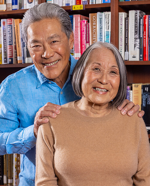 Senior man with his hands on the shoulders of a senior woman in front of a bookshelf in the library