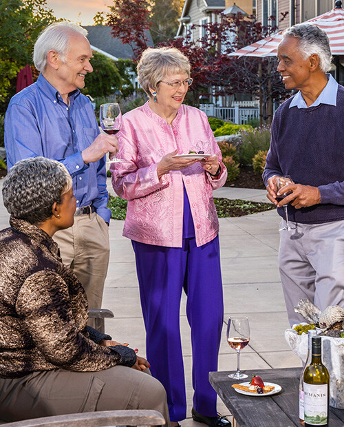 Two senior men and two senior women holding wine glasses and small plates of food on a patio