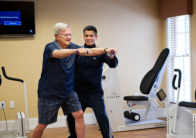 Senior man using light weights and working with a personal trainer in the community fitness center