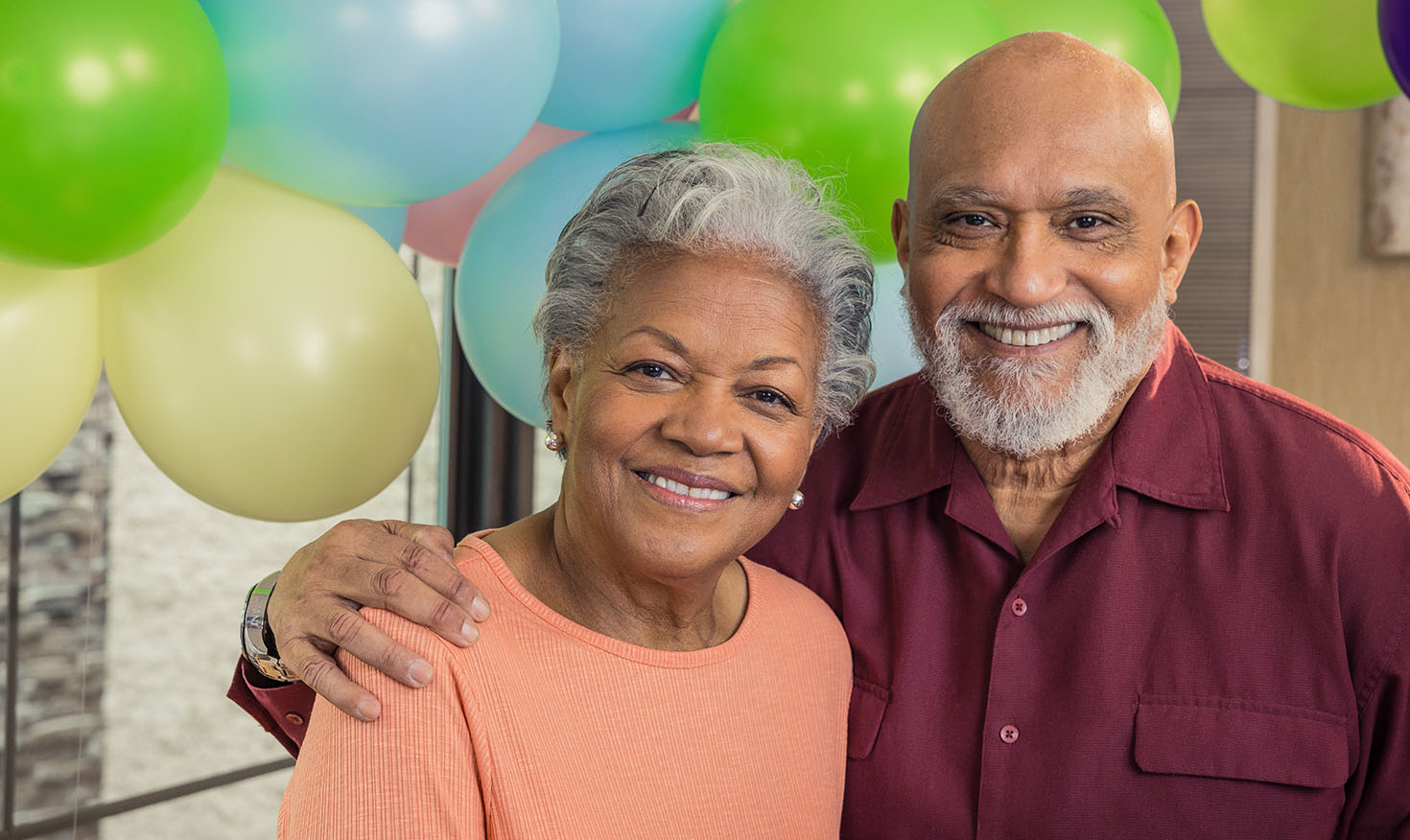Smiling senior man with his arm around a senior woman standing in front of balloons