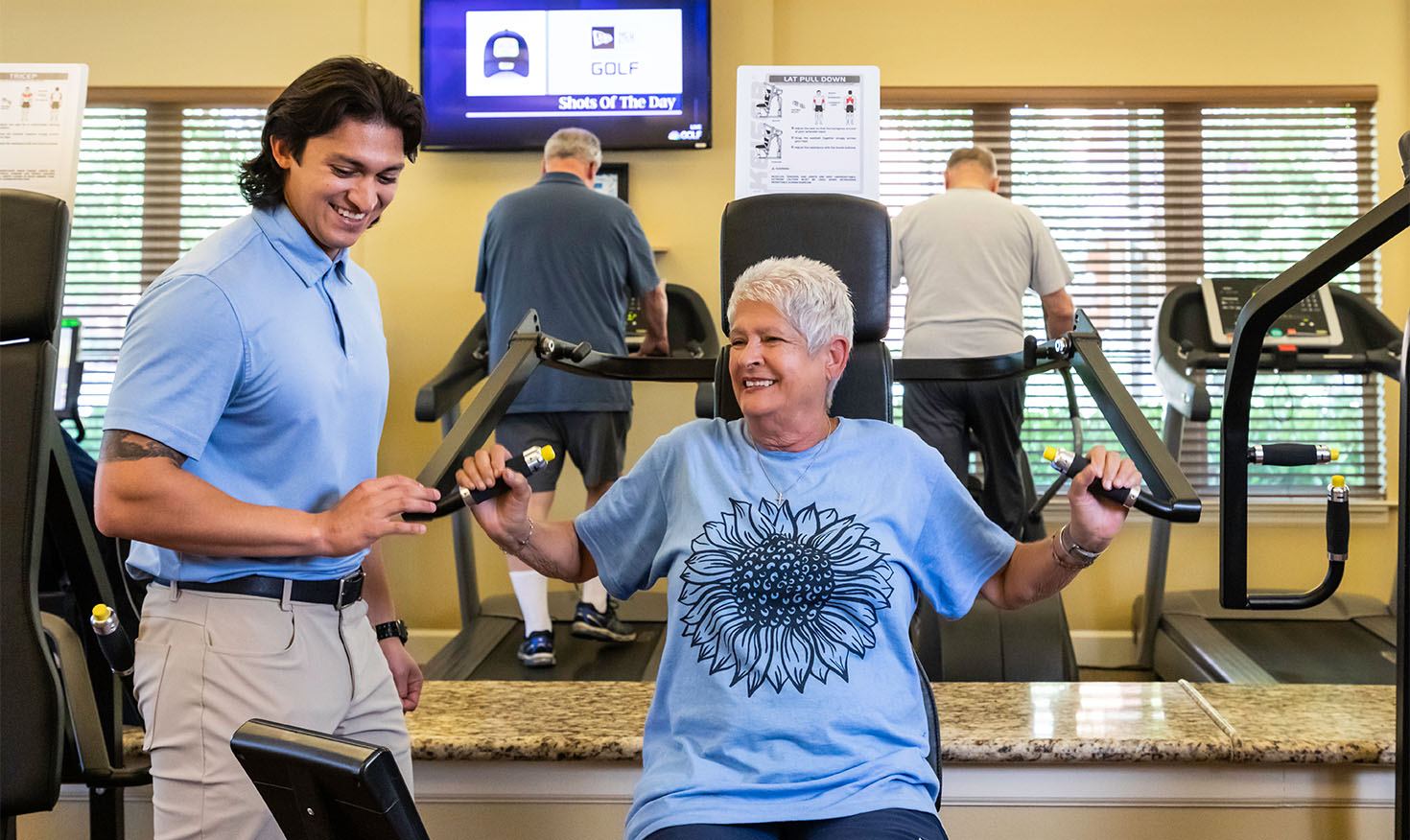 Senior woman using weight machine in the fitness center with a personal trainer