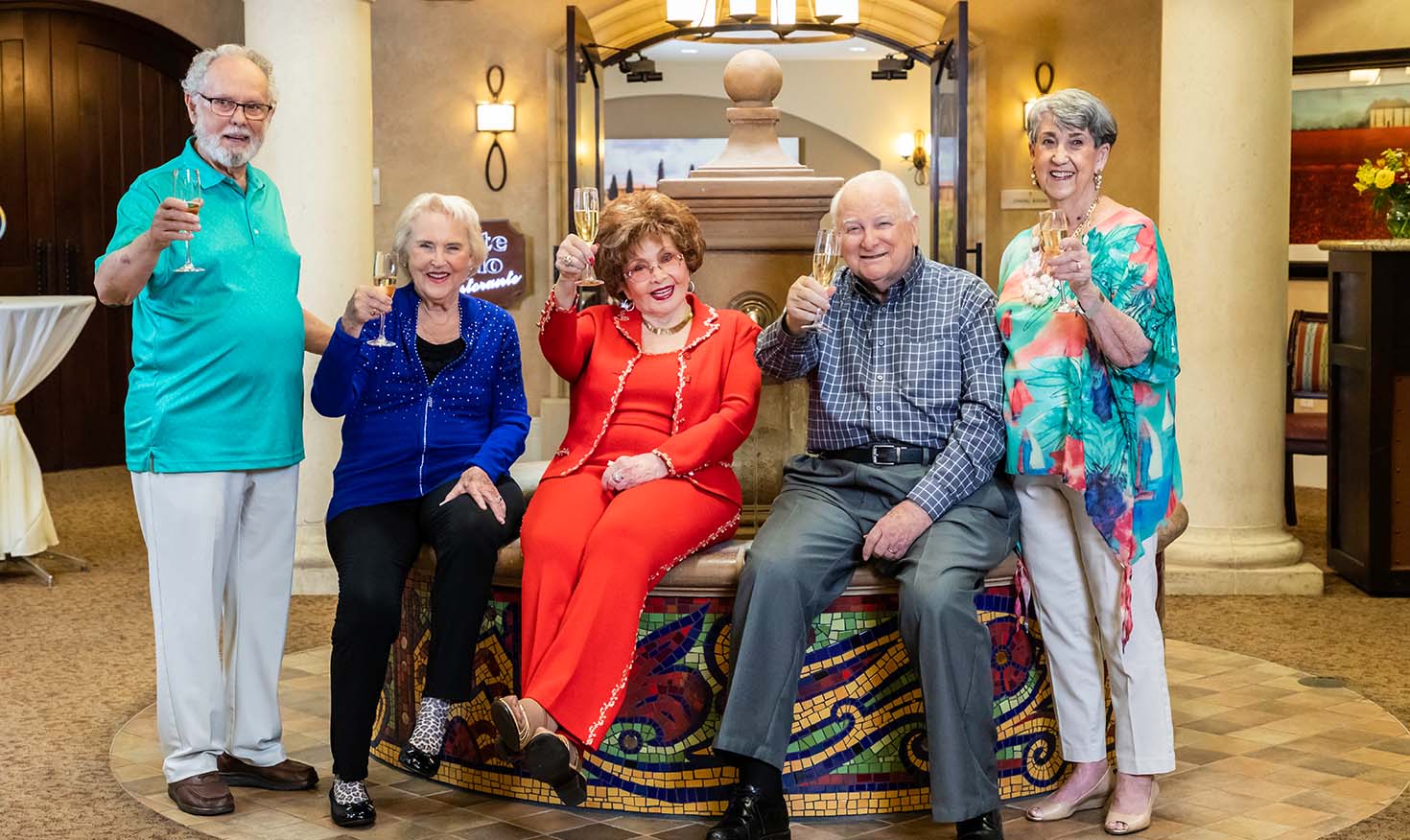 Group of five seniors by the fountain toasting the camera with Champagne glasses