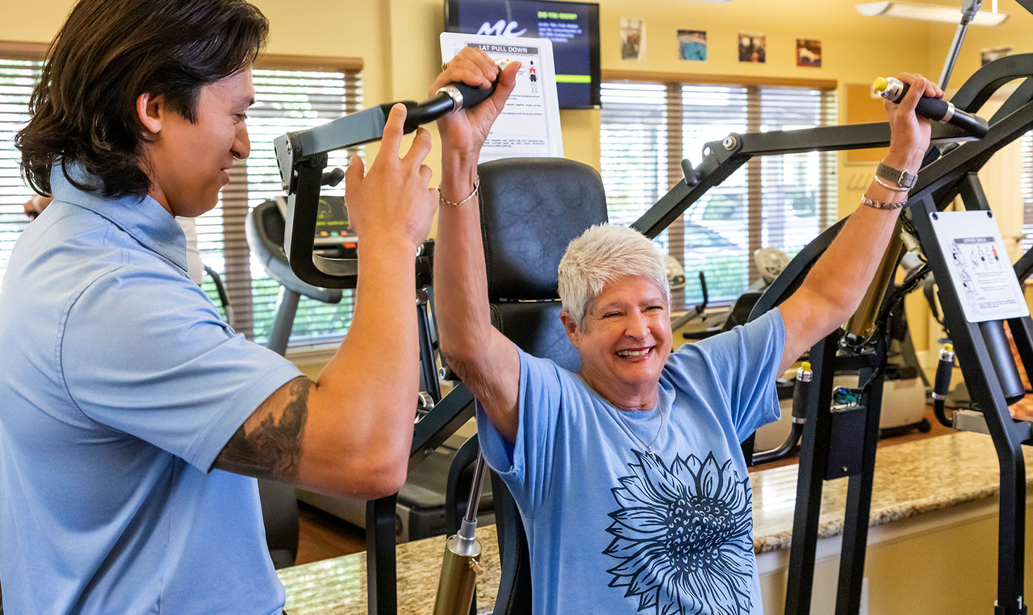  Senior woman using weight machine in fitness center with the assistance of personal trainer