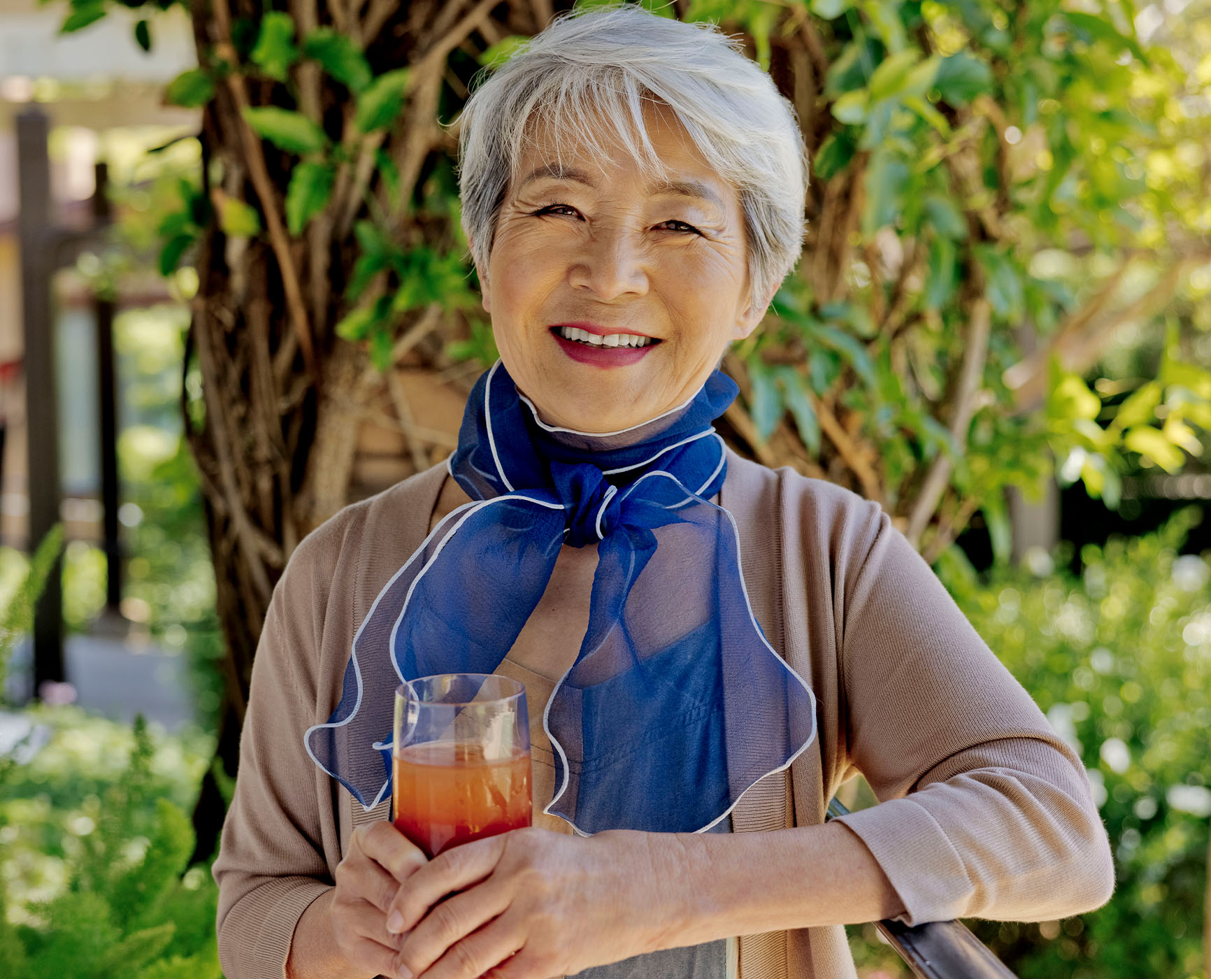 Senior woman wearing a blue scarf standing outside and holding a drink 