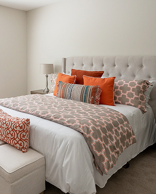 Bed with a tufted headboard and orange accent pillows in an apartment 