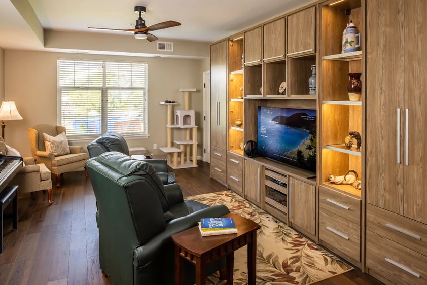 A living room with a pair of green leather chairs in front of an TV on a built-in shelf, a piano and a cat tower in an apartment