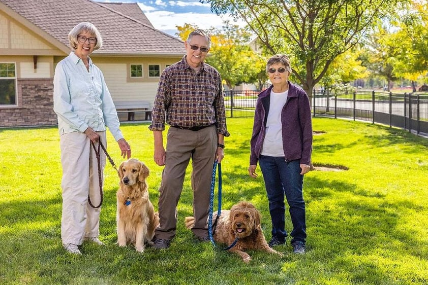 Two senior women and a senior man with two dogs standing in the dog park at The Terraces of Boise