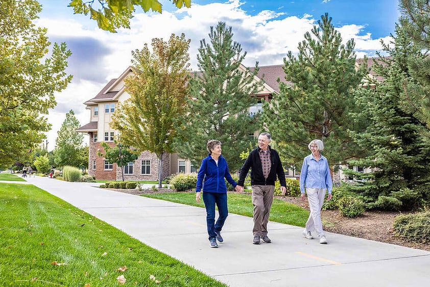 Senior couple holding hands and walking next to a senior woman through The Terraces of Boise