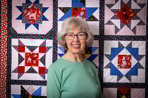 Smiling senior woman standing in front of a quilt