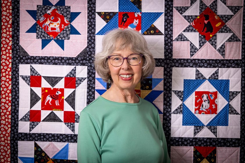Smiling senior woman standing in front of a quilt