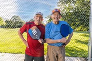 Two senior men holding up pickleball paddles