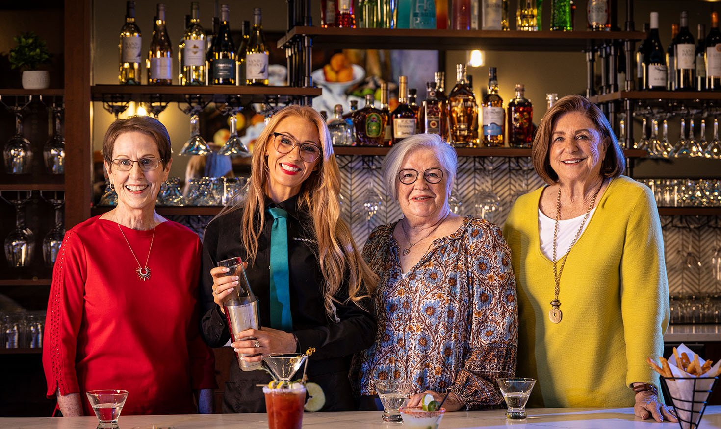 Three senior women and a female mixologist at a bar during a cocktail making class